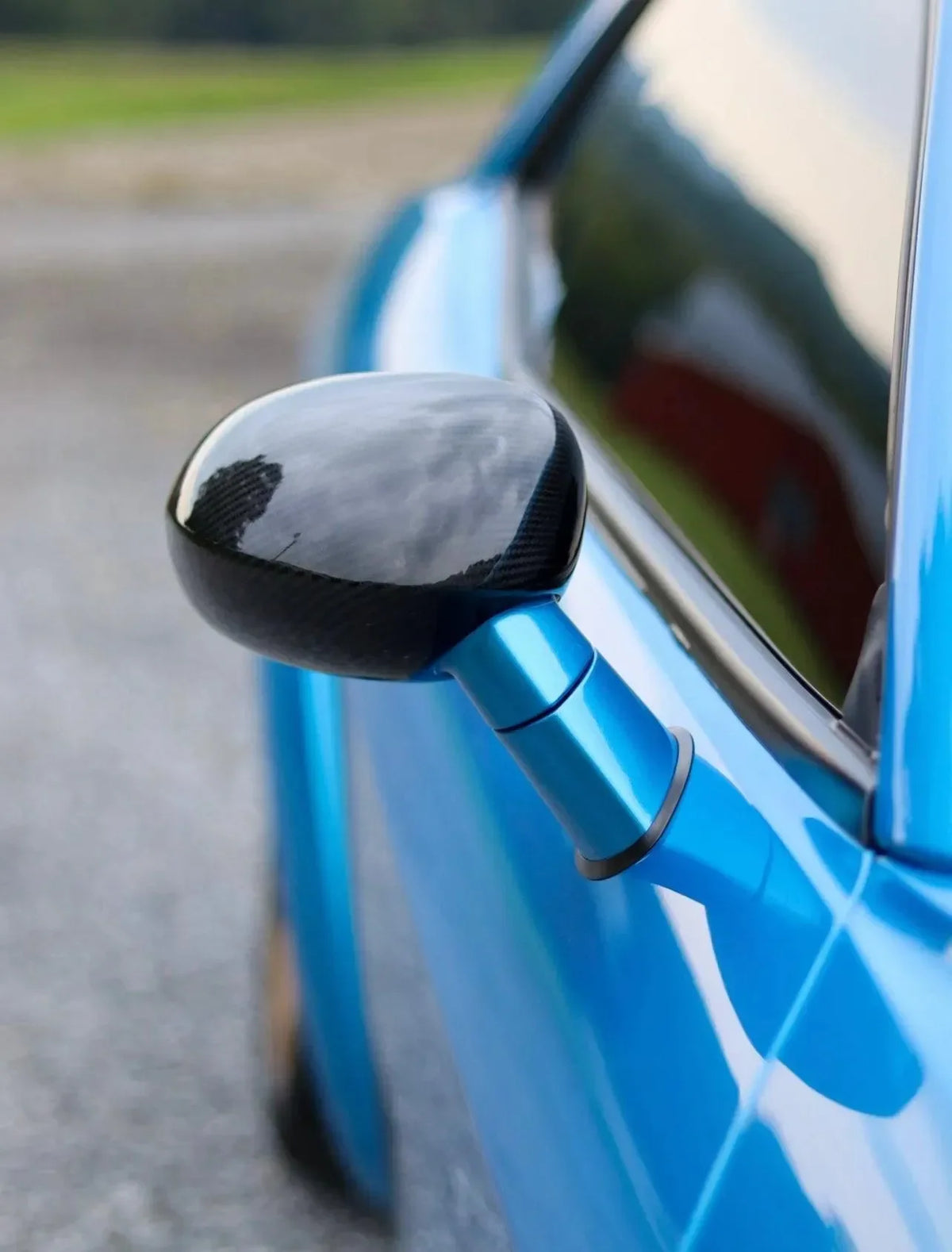 Glossy carbon fiber side mirror on a blue performance car, showcasing real carbon fiber exterior styling.