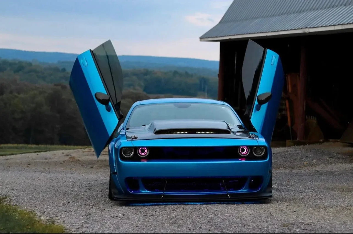 Blue Dodge Challenger with carbon fiber hood and custom doors, parked near barn with scenic hills