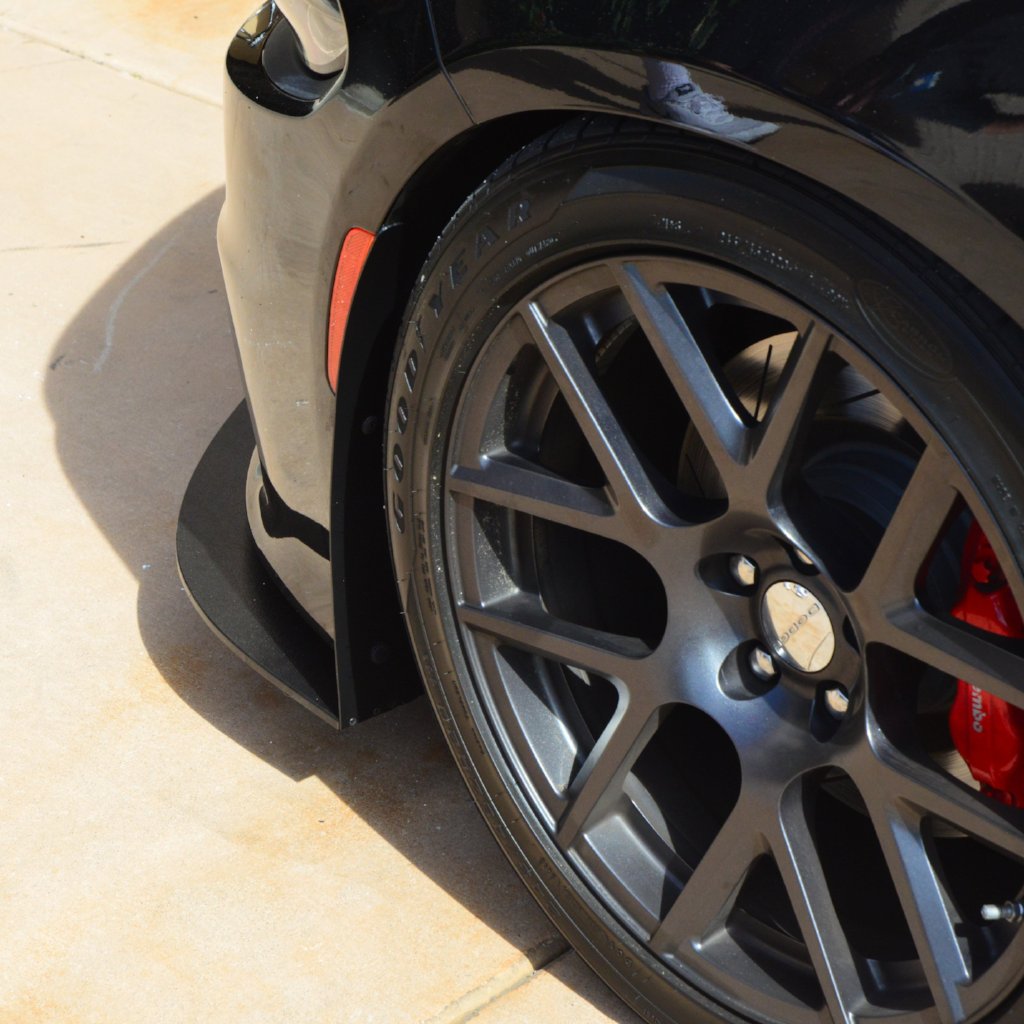 Close-up of a car wheel with a black rim and red brake caliper on a tiled floor.