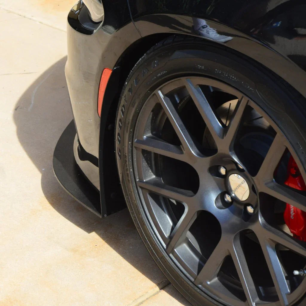 Close-up of a car wheel with a black rim and red brake caliper on a tiled floor.