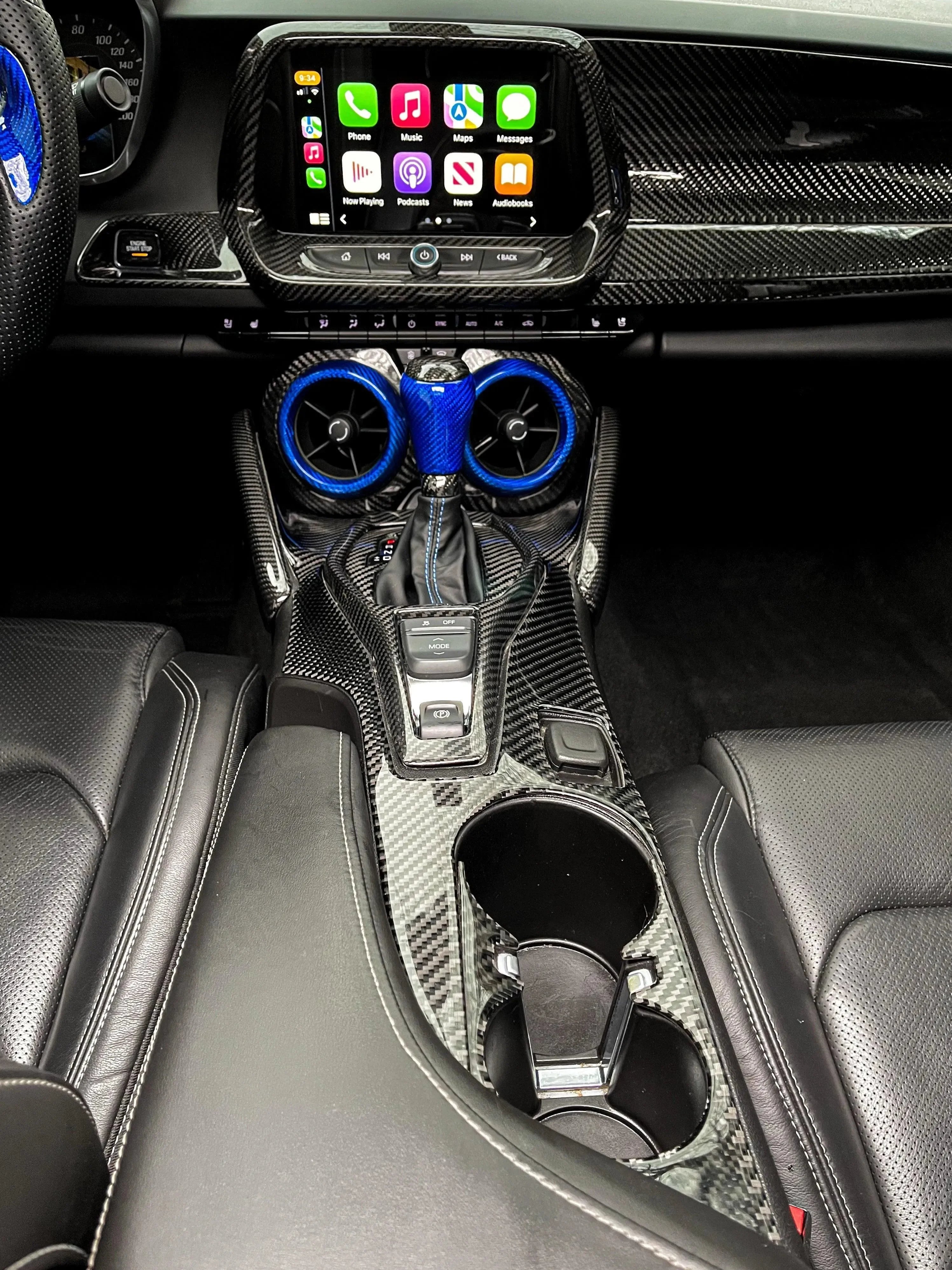 Carbon fiber interior trim with blue accents on gear shifter and vents, enhancing car dashboard and center console.