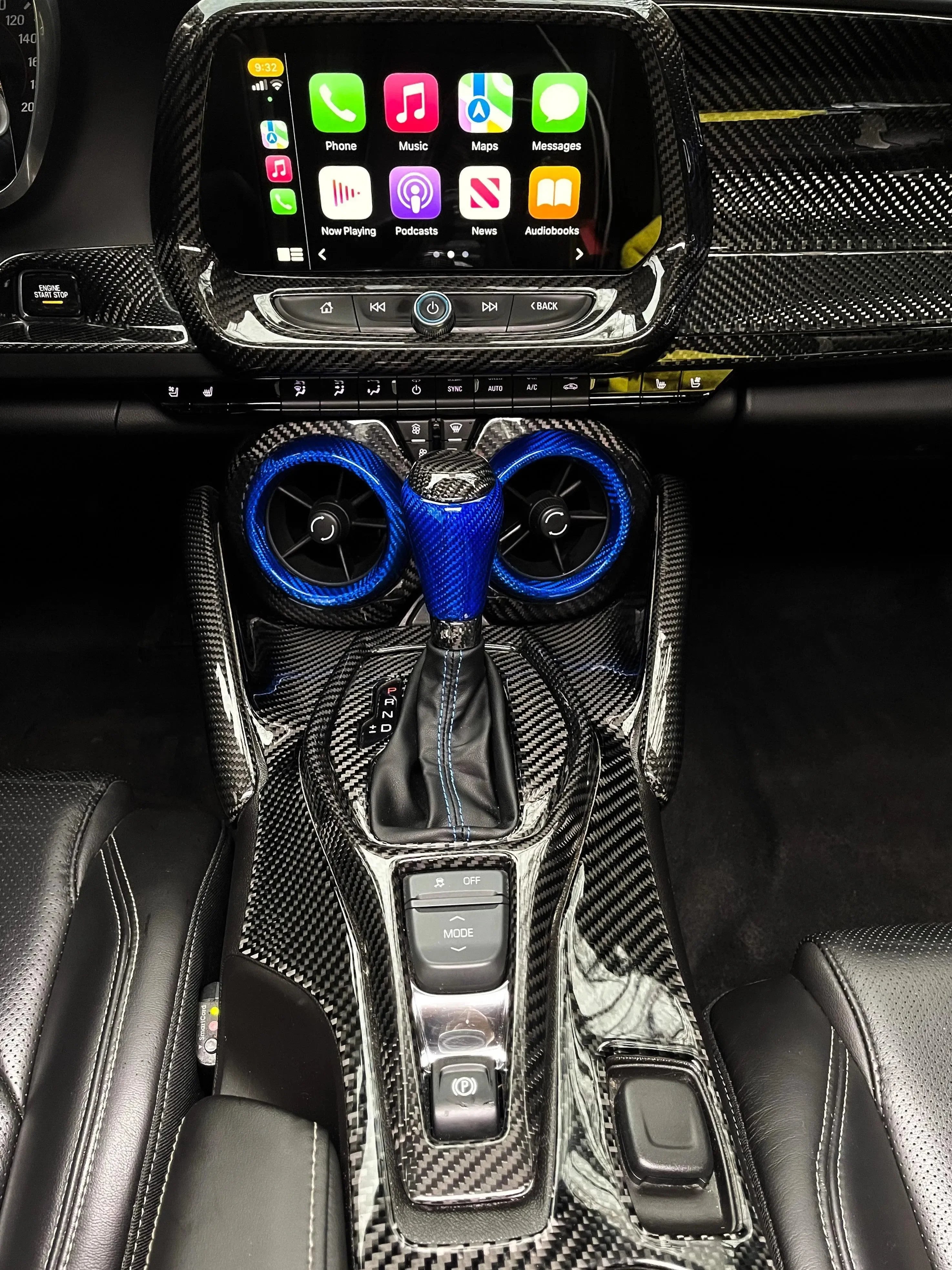 Carbon fiber interior with blue-accented gear shifter and air vents, Apple CarPlay displayed on touchscreen.