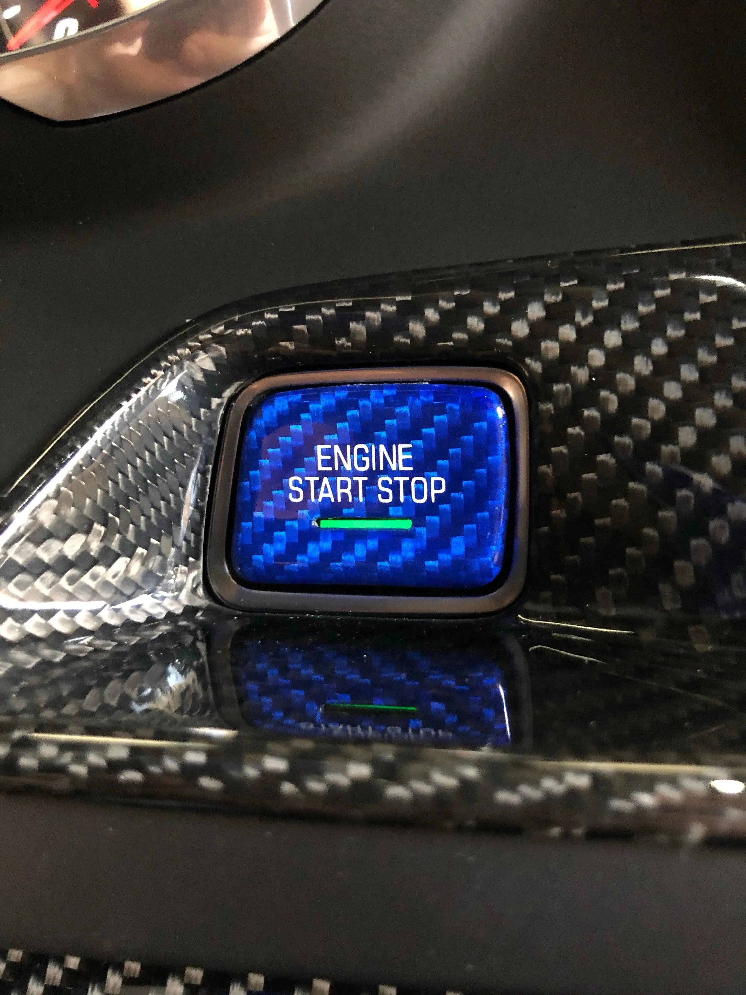 Blue carbon fiber engine start stop button in car interior