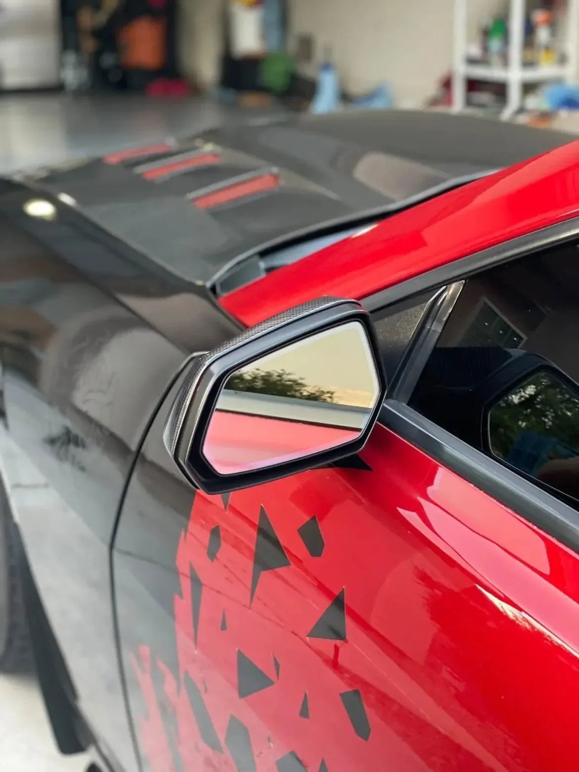 Carbon fiber side mirror and hood on red muscle car, custom geometric graphics, garage setting