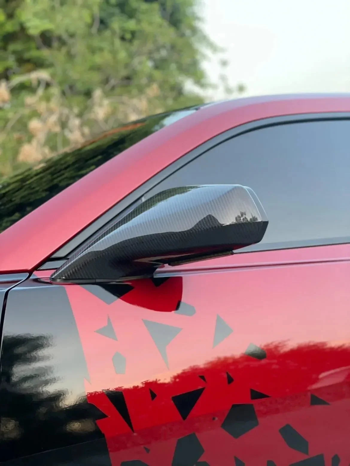 Real carbon fiber side mirror on red sports car with geometric decal