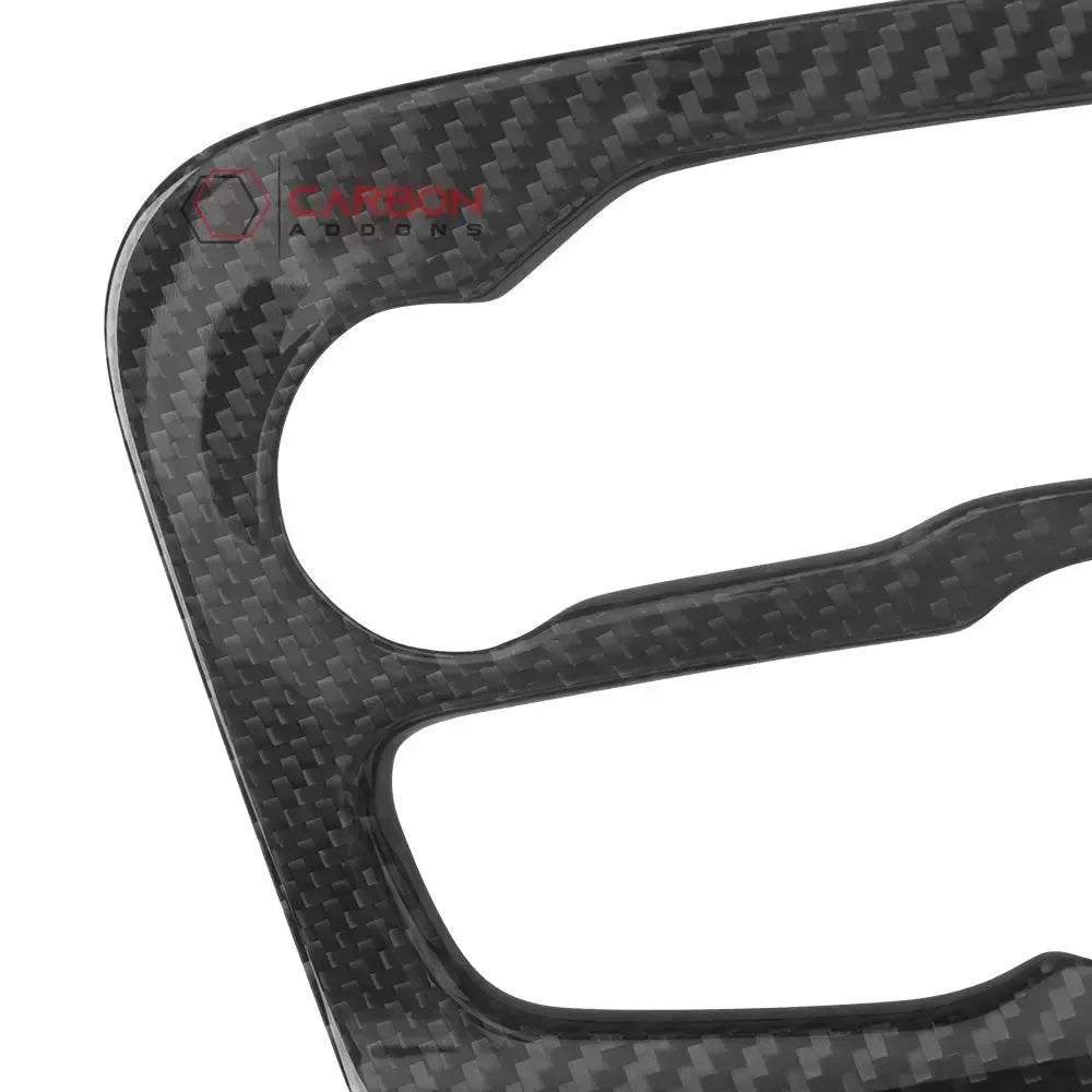 Real carbon fiber automotive trim with glossy weave pattern and branded logo detail