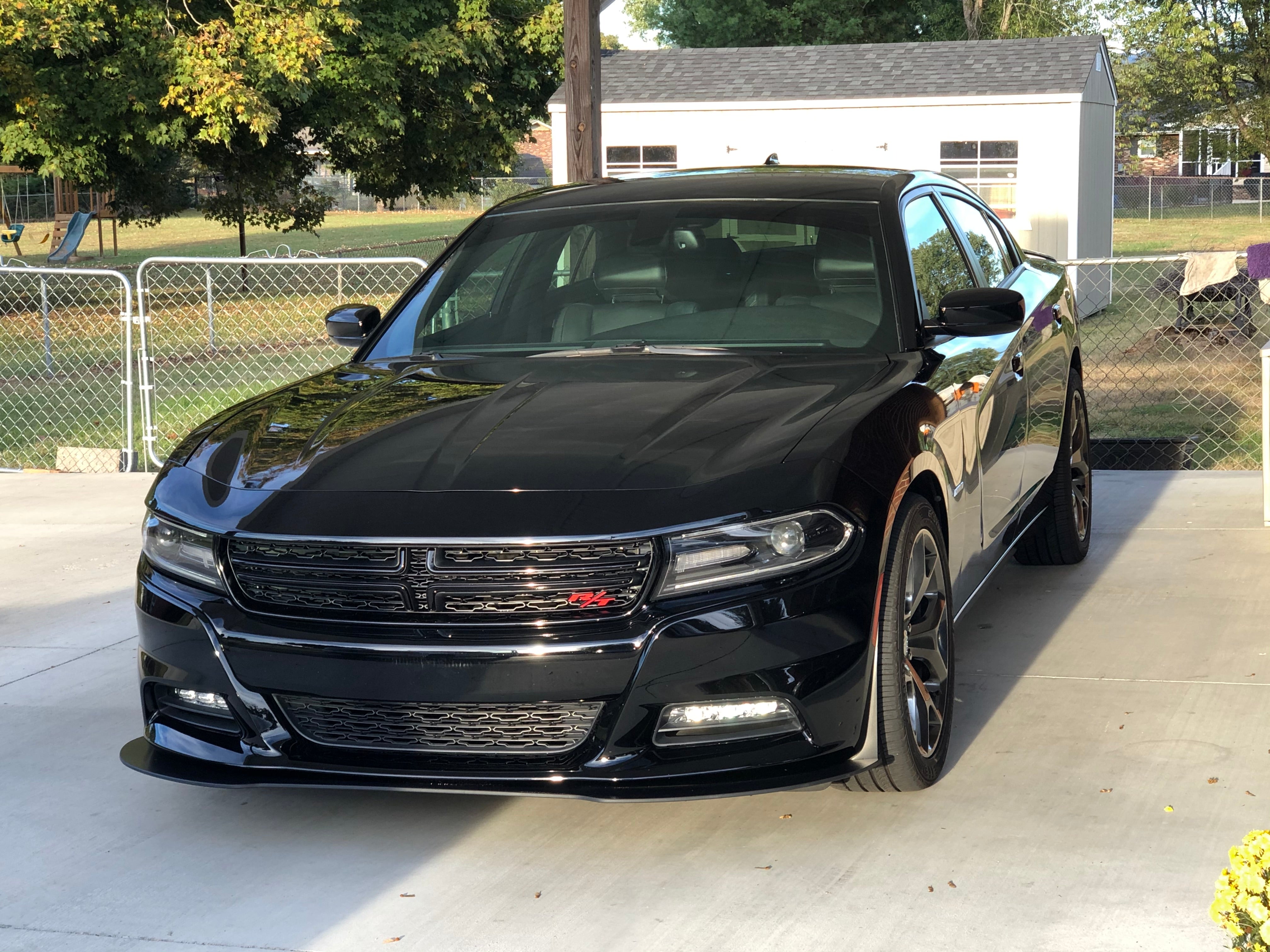 Black Dodge car parked on a driveway with a house and trees in the background