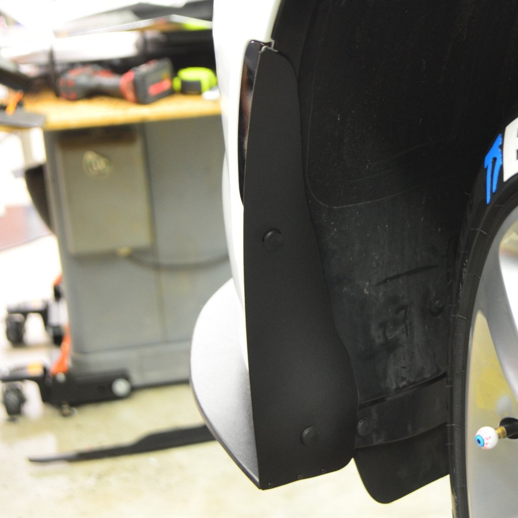 Close-up of a car tire with a black mud flap in a workshop setting