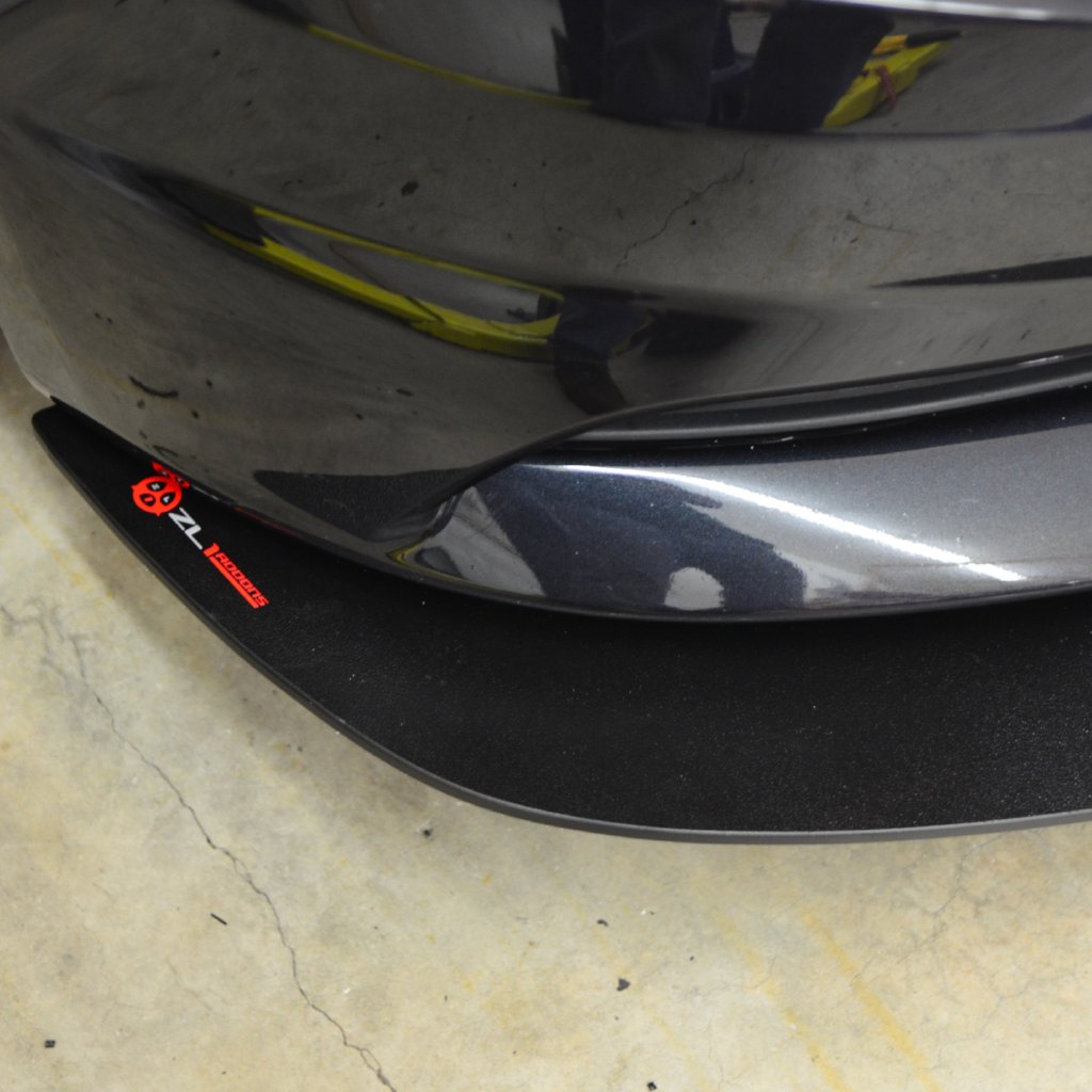 Close-up of a car's front bumper with a visible brand logo on a concrete surface.