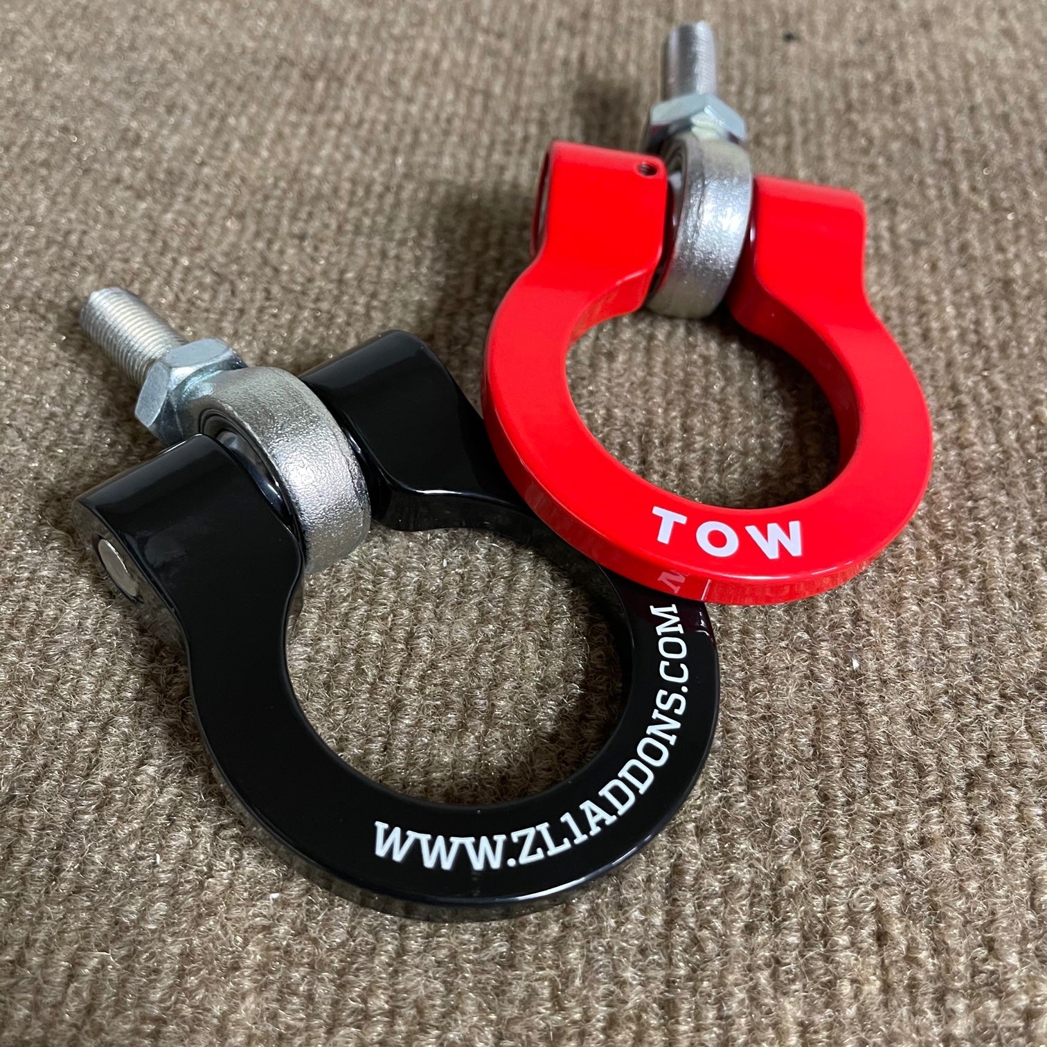 Two towing hooks, one red and one black, with visible branding on a textured surface.
